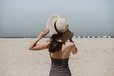 Rear view of woman standing at beach against clear sky
