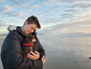 Young woman with dog standing on beach against sky