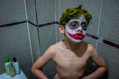 Shirtless boy with face paint standing in bathroom