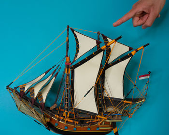 Person holding sailboat in sea against blue sky