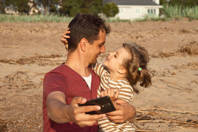 Father and daughter embracing while doing selfie standing outdoors