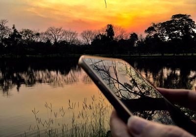 Reflection of silhouette trees in lake against orange sky