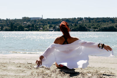 Back view of carefree woman with arms outstretched relaxing at the beach in summer day.