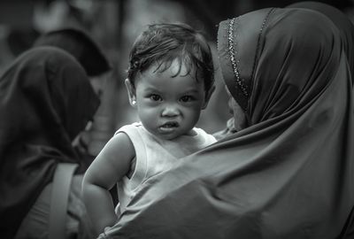 Rear view of mother carrying cute daughter making face while standing outdoors