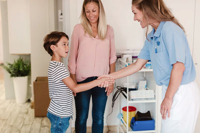 Smiling pediatrician shaking hands with boy by mother standing in doctor's office