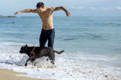Playful shirtless man with dog at beach during vacation