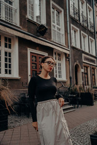 Portrait of young woman standing against building