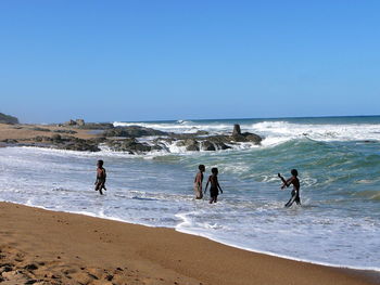 Boys playing in sea on shore against clear sky