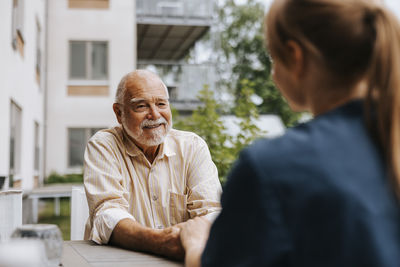 Smiling senior man holding hands of female nurse while sitting in back yard