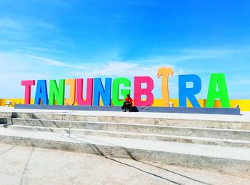 Man sitting by colorful text on steps during sunny day