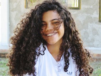 Portrait of smiling teenage girl with curly hair sitting against house