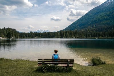Rear view of person sitting on bench against lake