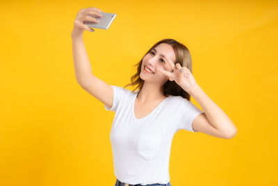 Young woman using mobile phone against yellow background