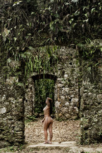 Full length of naked young woman standing against old ruins