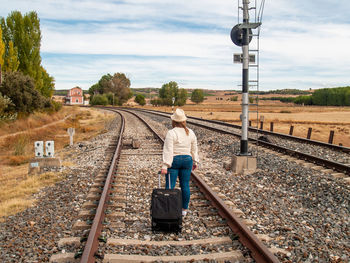 Rear view of woman walking with luggage on railroad track