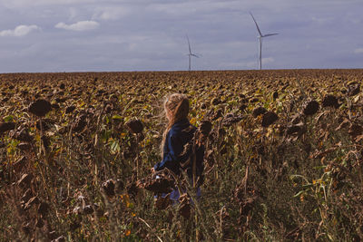 Child girl in sunflowers. scenic view of field against sky.wind turbines background eco green energy