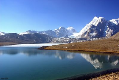 Scenic view of lake and snowcapped mountains against clear blue sky