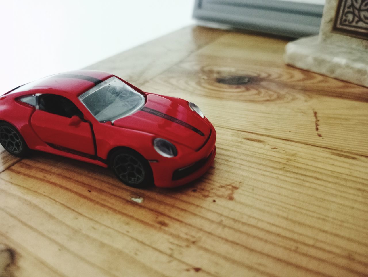 car, toy car, toy, red, land vehicle, wood, vehicle, childhood, indoors, scale model, motor vehicle, model car, wheel, table, automobile, mode of transportation, flooring, transportation, sports car, close-up, supercar, still life, selective focus