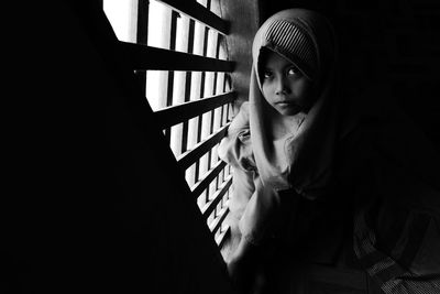 Girl in headscarf standing by window