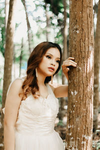 Portrait of young woman standing against tree trunk