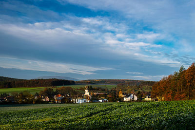 Scenic view of field by houses against sky