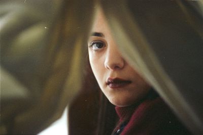 Portrait of young woman seen through curtain