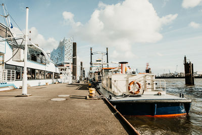 Sailboats moored on harbor by buildings in city against sky
