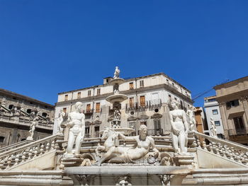 Low angle view of statues on building against blue sky