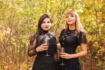 Young women with drinks standing against trees