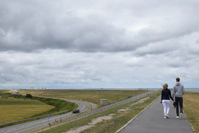 Rear view of people walking on road against sky