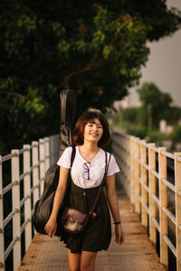 Portrait of woman standing on footbridge against trees