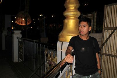 Portrait of young man standing against railing at night