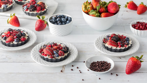 Sweet mixed berry cheesecake tarts with bowls of extra berries.