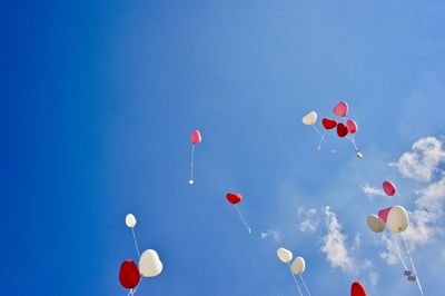 Low angle view of heart shape balloons flying against blue sky