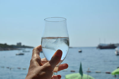 Close-up of hand holding glass against sea