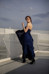 Portrait of woman in dress standing in balcony against sky