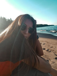 Portrait of woman wearing sunglasses at beach against sky