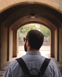 Rear view of man with backpack standing against built structure