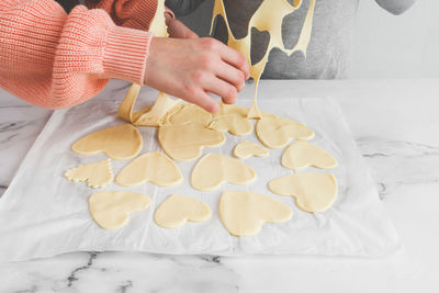 Hands of a young caucasian girl of a baker's sister separating raw dough from cut out hearts.