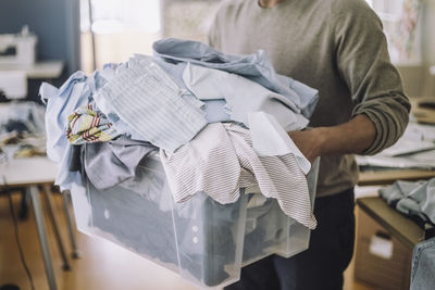 Midsection of male fashion designer holding recycled clothes in container