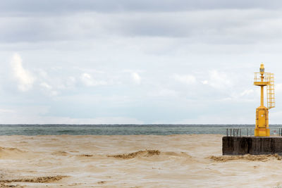 Yellow lighthouse at beach against cloudy sky