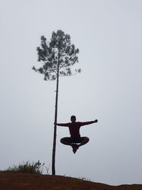 Man with arms outstretched on field against clear sky