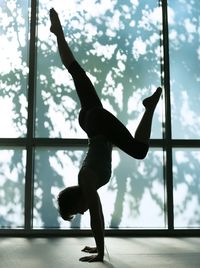 Side view of woman practicing handstand by window