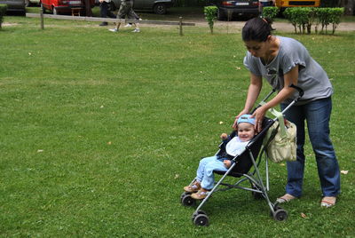 Mother adjusting daughter cap in baby stroller at park