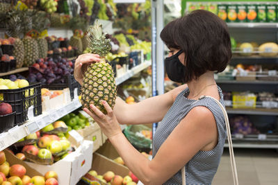 Woman buyer in a protective medical mask chooses a pineapple store. person