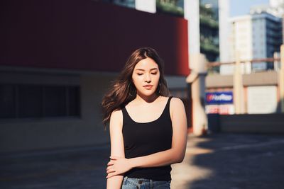 Young woman looking down while standing on road against buildings in city