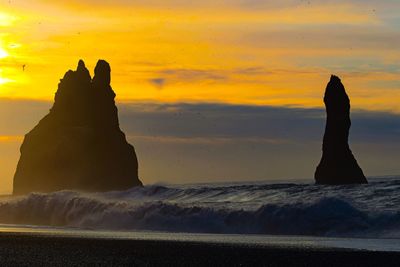 Silhouette rock formation on beach against sky during sunset