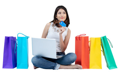 Young woman using phone while sitting against white background