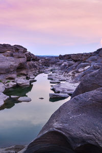 Rock formation in lake against sky during sunset