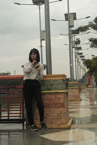 Full length portrait of young woman standing against sky